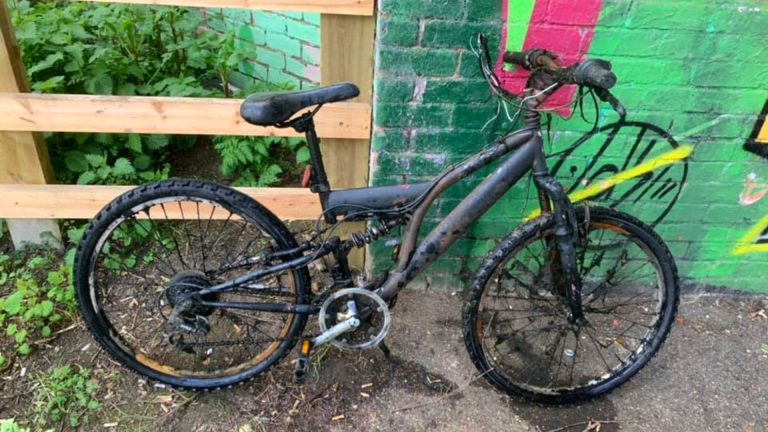 bicicletă corodată în stare deplorabilă, sprijinită de un zid