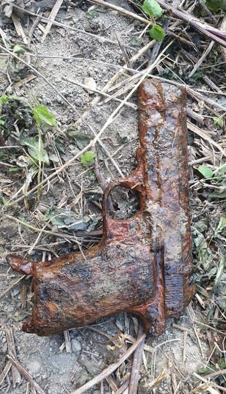 Pistol acoperit de un strat gros de rugină, în iarbă